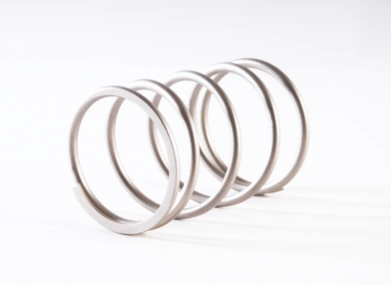 Vista en perspectiva de un muelle helicoidal de acero inoxidable con espiras anchas y regulares, resaltando el acabado metálico satinado sobre un fondo blanco limpio.