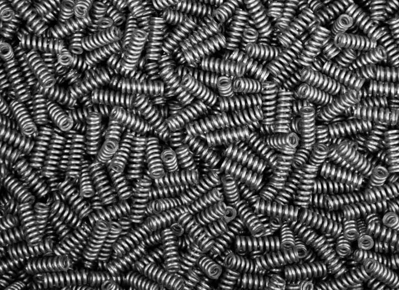 Primer plano de una gran cantidad de muelles helicoidales de acero pequeños amontonados de forma aleatoria, mostrando una textura metálica densa y uniforme.