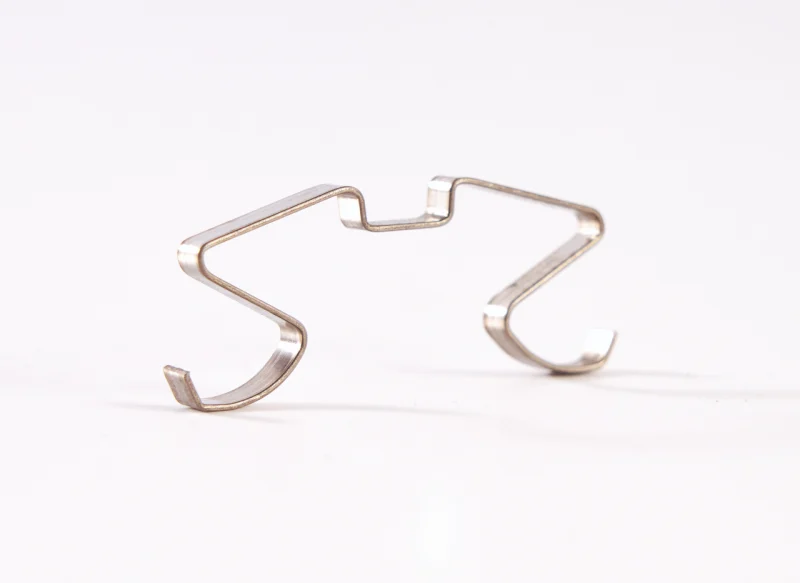 Pieza metálica de fleje de acero conformado con diseño simétrico de precisión sobre fondo blanco.