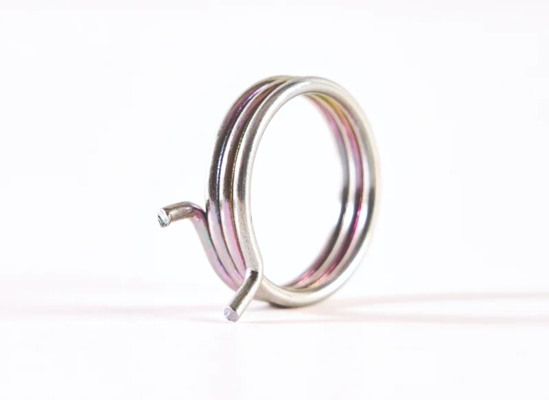 Composición de varios muelles de torsión de distintos tamaños sobre fondo blanco, mostrando modelos de torsión doble, muelles con brazos largos acodados y micromuelles de precisión en diferentes acabados metálicos.