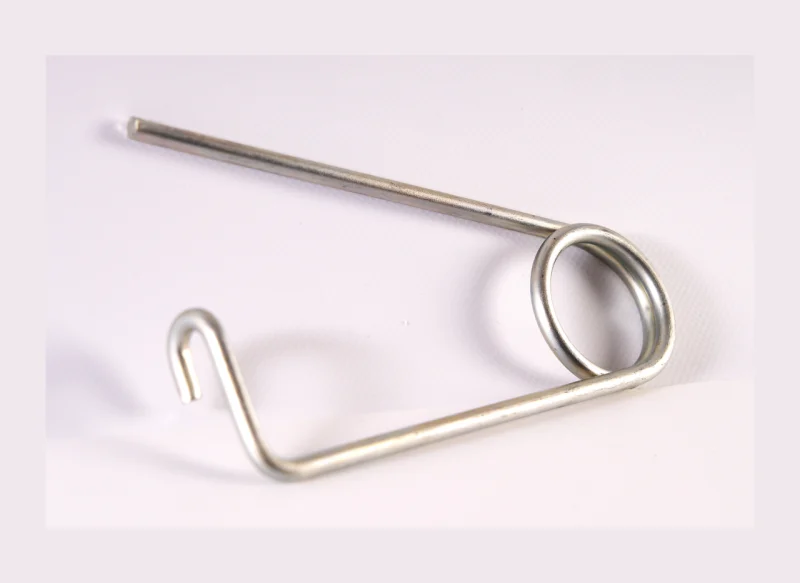 Muelle de torsión de acero de gran calibre sobre fondo blanco, con un cuerpo helicoidal corto de hilo grueso y dos brazos metálicos largos, uno de ellos con una ligera angulación en el extremo.