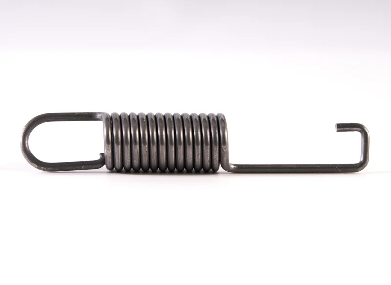 Muelle de tracción de acero industrial con terminales mixtos: un ojal alargado en el extremo izquierdo y un gancho corto en forma de J en el derecho, sobre fondo blanco.